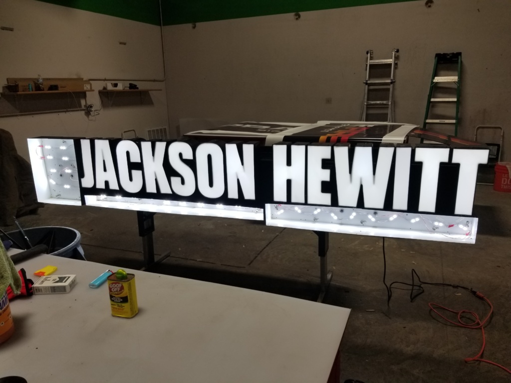 channel » Prairie Fire Signs & Graphics Front-lit channel letters for "Jackson Hewitt" in a workshop, showcasing how light shines through the face of the letters for clear nighttime visibility.