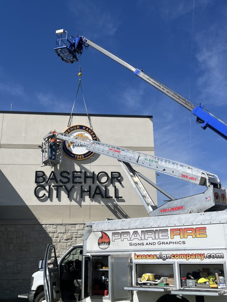 Professional sign company team installing a new exterior business sign on a building to enhance branding and visibility in a competitive Kansas market.